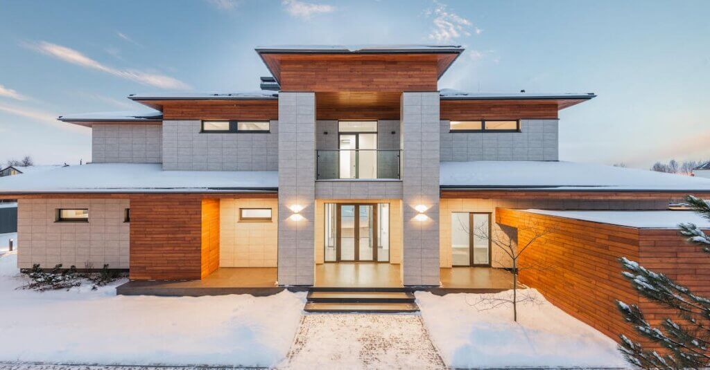 Backyard view of new modern luxurious cottage house with stone and wooden facade and illumination in winter countryside