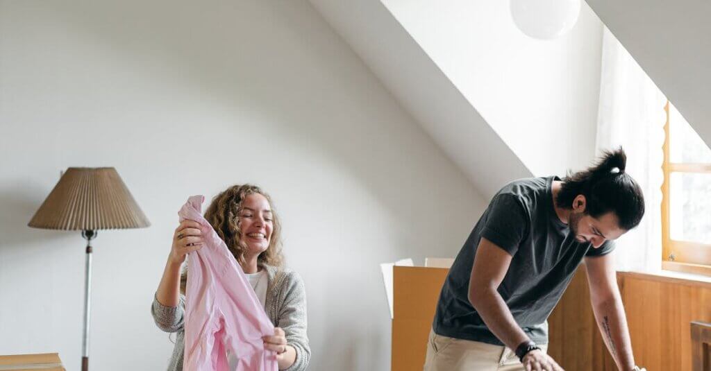 Full body happy young couple packing suitcases and carton boxes while preparing to move into new apartment in empty bedroom on sunny day