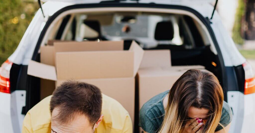 Tired couple sitting on car luggage boot